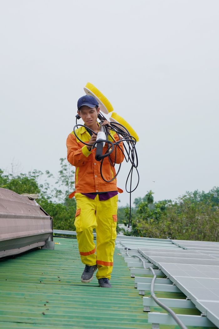 Services Asian technician walking on a rooftop carrying solar installation equipment in uniform.