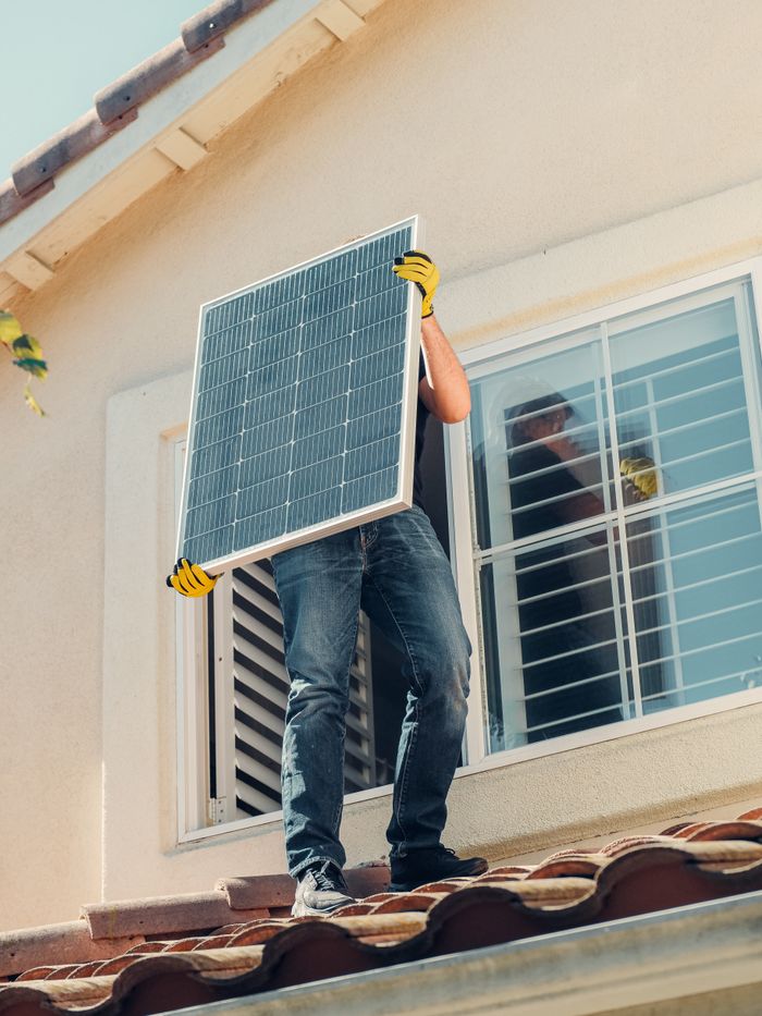 Services Technician carrying a solar panel on a rooftop for installation, promoting renewable energy.